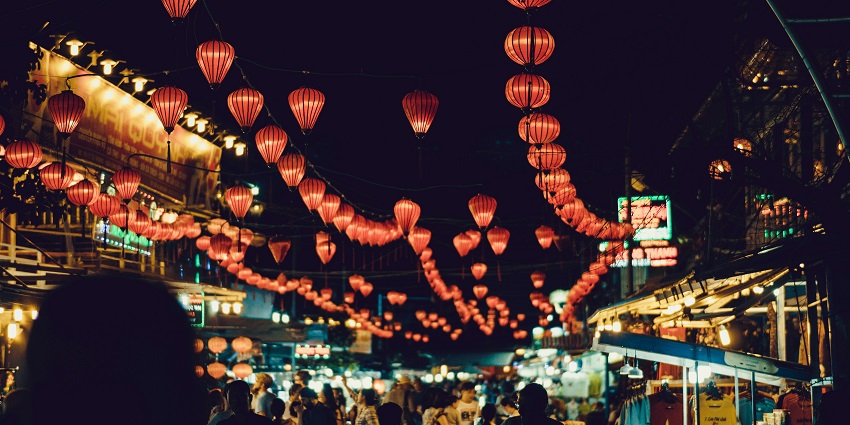 People walking between stalls under hanging Chinese lanterns in a street market