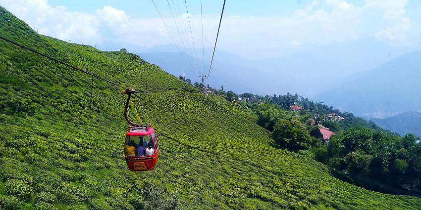 Darjeeling ropeway cabins are moving over lush green hills under a clear daytime sky.