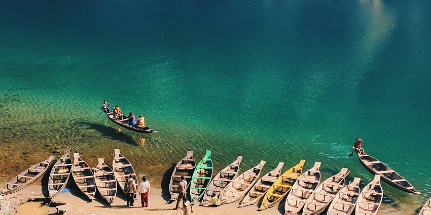 Dawki River with a greenish water body, multiple boats on the river and green mountains.