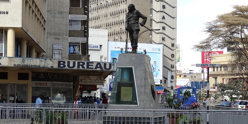 A statue of Dedan Kimathi in Nairobi with city buildings visible in the background.