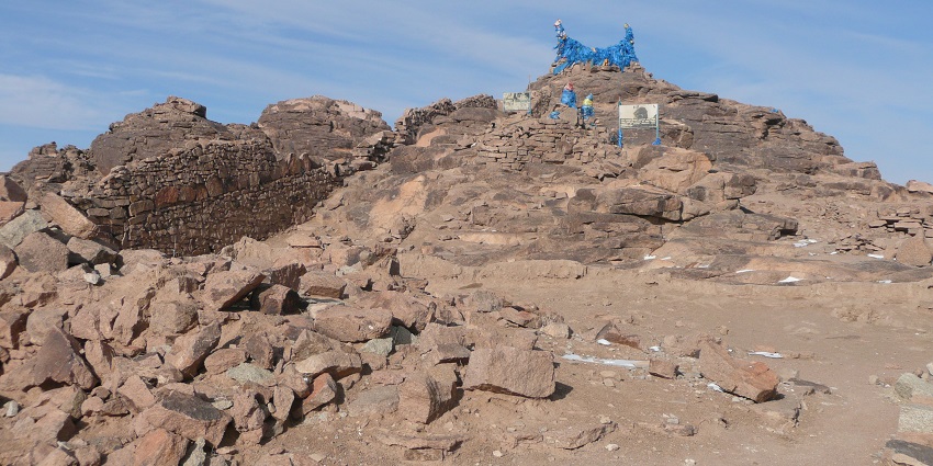 Monastery ruins in Magnolia with multiple rocks, a signboard at a distance and blue flags