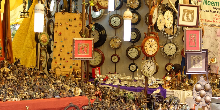 Clock shop in Delhi Haat INA with small statues, paintings, hanging clocks, and lights.
