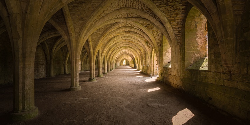 Narrow stone tunnels with arched ceilings and rustic walls beneath the old monastery structure.
