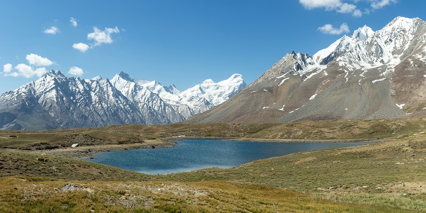 Baralacha Lake with still blue waters surrounded by snow-capped mountains and rocky terrain