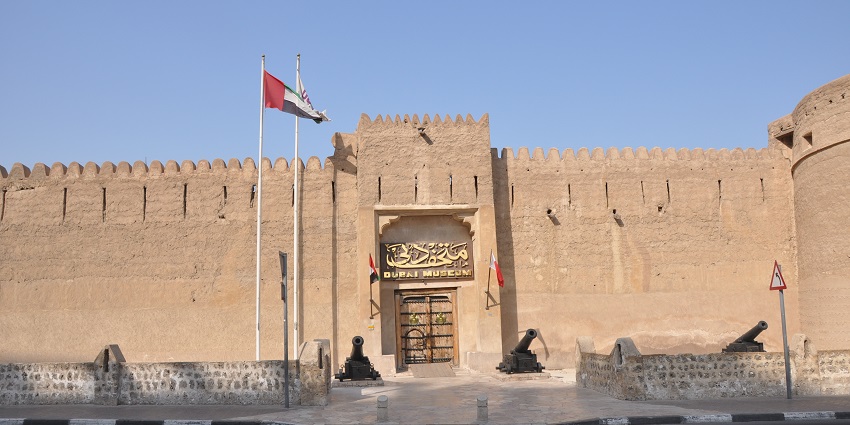 Al Fahidi Fort in Dubai, a historic sand-colored structure with watchtowers and flags.