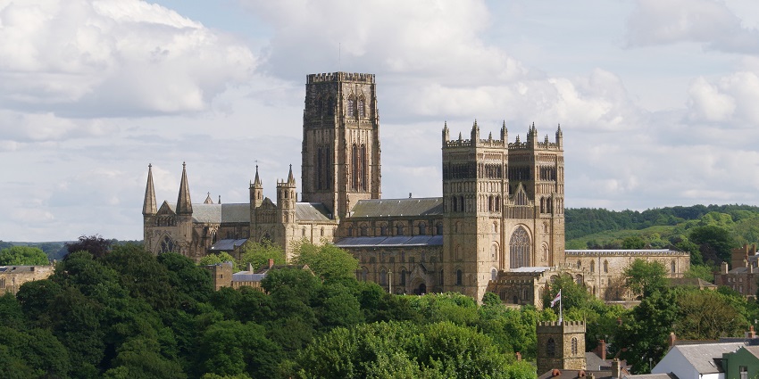 Durham Cathedral with traditional Gothic architecture, a flag and surrounded by greenery.