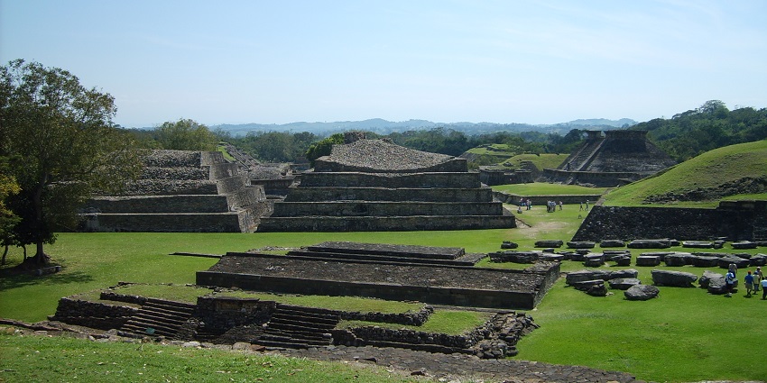 Ruins of El Tajin with broken pyramids, rocks on the ground, green plains and distant people