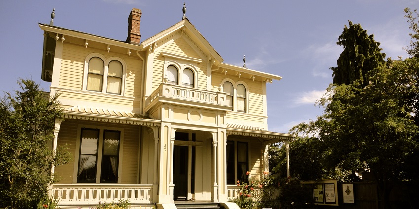 Yellow Victorian-style house with arched windows, front porch, and garden-lined walkway.