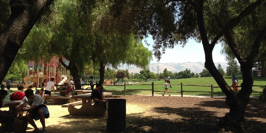 Playground of Emma Prusch Farm park with distant swings for kids and people sitting.