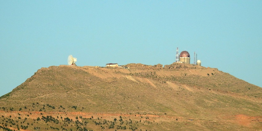 Radar and observatory station atop a mountain peak with a clear blue sky in the background.