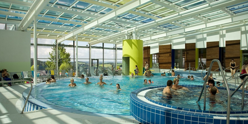 Outdoor swimming pool at a resort with clear water, surrounded by trees and greenery.