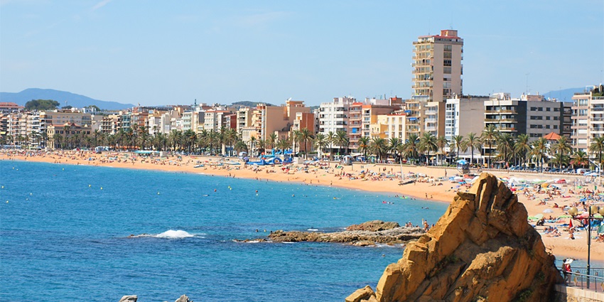 Tourists sunbathing and swimming on the sandy beaches of Lloret de Mar with a vibrant summer atmosphere, one of the things to do in Costa Brava.