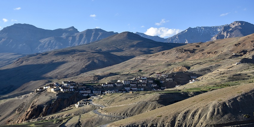 A cluster of whitewashed houses on a barren hillside beneath rugged Himalayan mountain peaks.