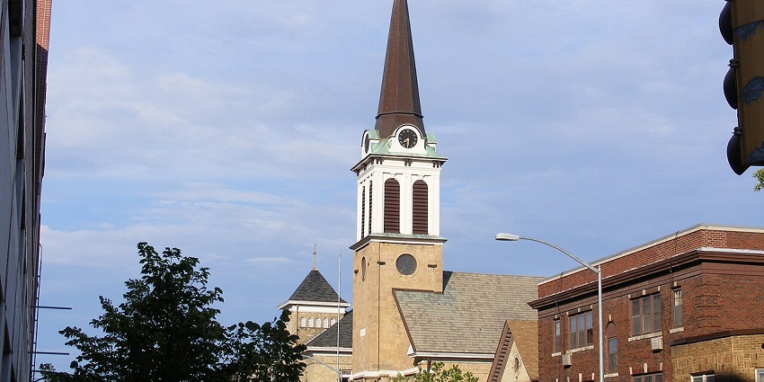 St. Joseph’s Church with its classic brick facade, arched windows, and tall steeple stands peacefully under a clear sky.