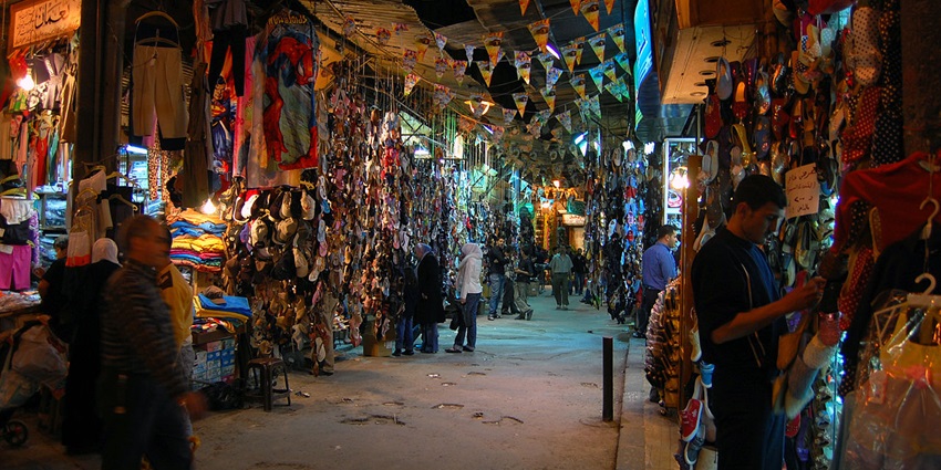 Busy night market with colorful clothes, shoes, and lights, filled with locals shopping and exploring stalls.