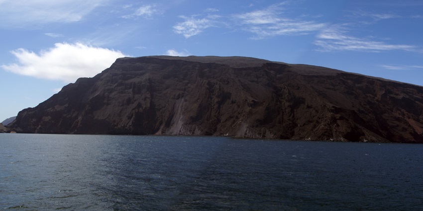A volcanic Fernandina island in Ecuador rises from the ocean under a bright blue sky