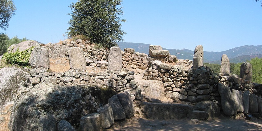 Filitosa with old carved stones, a stair made up of carved stone and green mountains in the back.
