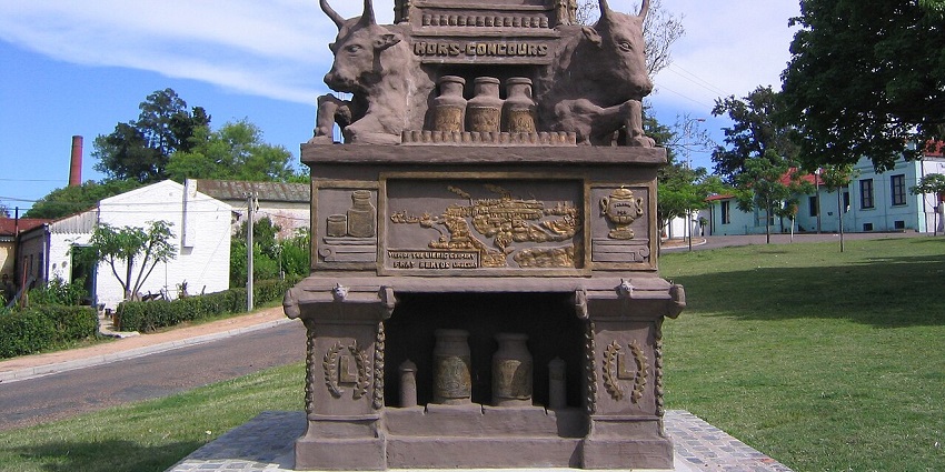 A historical monument featuring cattle and industrial motifs stands in a green park, a cultural place to visit in Uruguay.