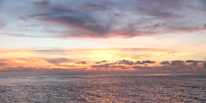 Beach with a large water body, small waves, vibrant orange-yellow clouds in the sky.
