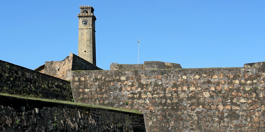 Galle Fort’s historic clock tower stands tall against a clear blue sky, with colonial buildings surrounding it in Sri Lanka.