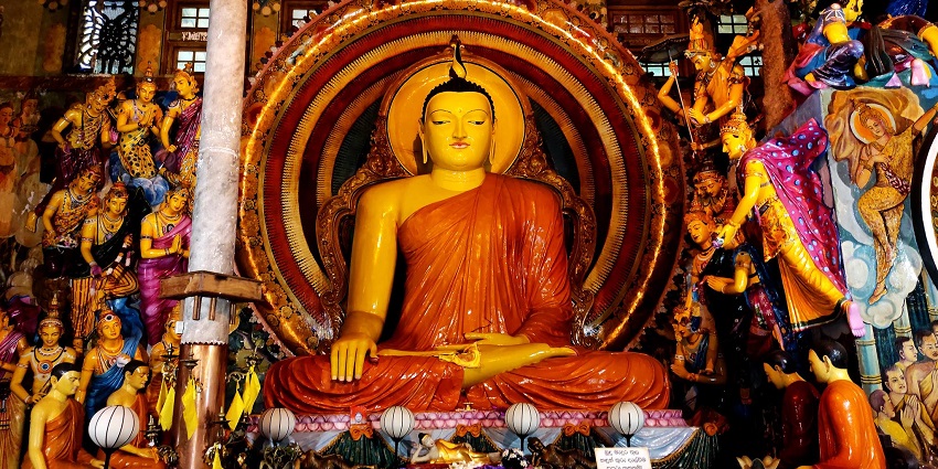 A golden seated Buddha statue inside Gangaramaya Temple, surrounded by decorations and traditional Sri Lankan architecture.