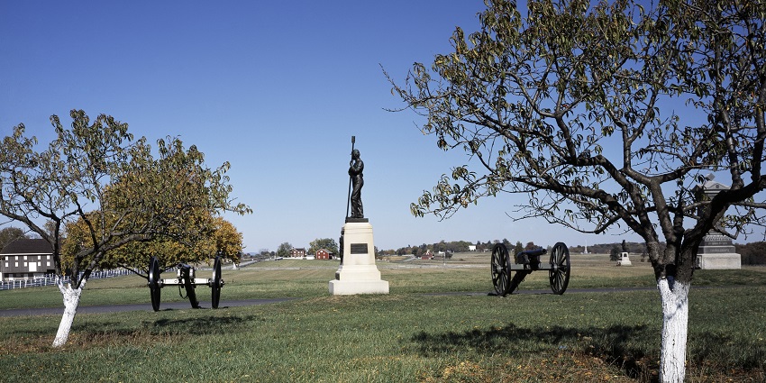Wide shot of Gettysburg Civil War battlefield monument with cannons under blue sky.