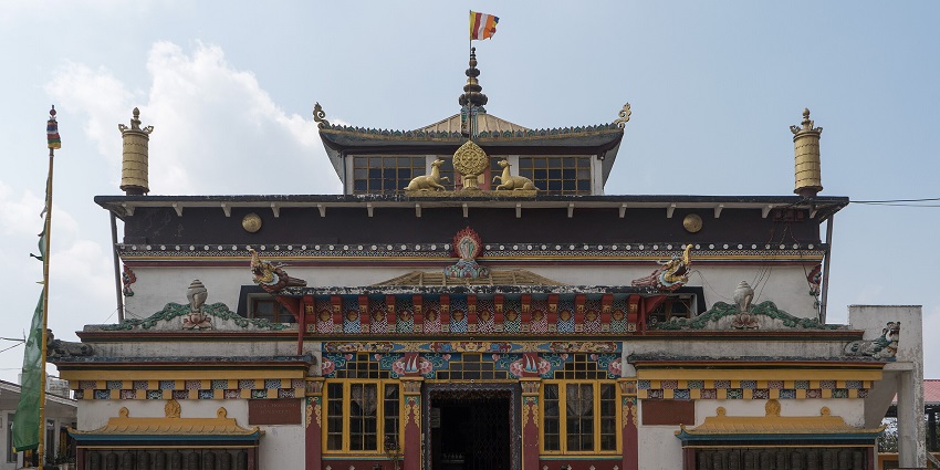 Front facade of Yiga Choeling monastery with traditional Buddhist architecture and a flag on top.