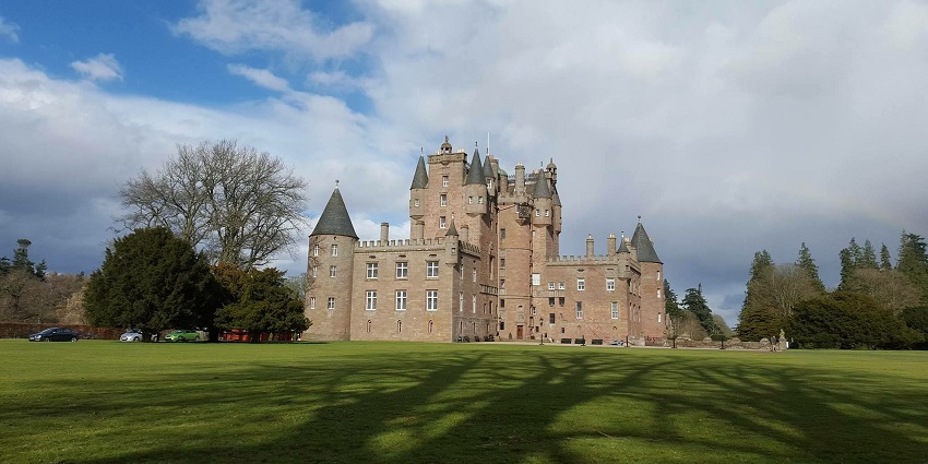 Glamis Castle with turrets and towers, set against a green lawn and cloudy sky, Scotland