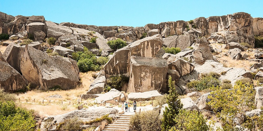 Prehistoric petroglyphs etched into rocky surfaces across a desert-like plateau, with Caspian Sea in the background.