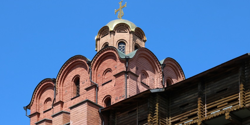 Golden-domed church tower with arched brickwork and wooden structure beneath a blue sky.