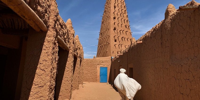 Grand Mosque of Agadez in niger with a tall sandstone minaret, blue gate and a man walking