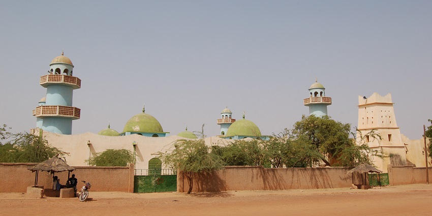 Great Mosque of Zinder with multiple tall minarets and people sitting in the hut-like structure