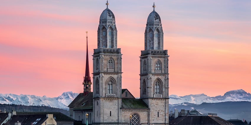 Double towers of Grossmünster Church in Zürich, Switzerland, standing tall against the evening sky with orange hues.