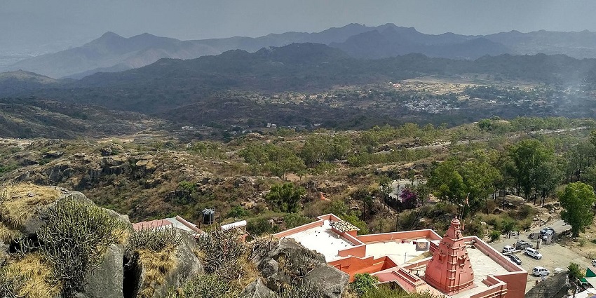 Guru Shikhar at the top of the Mount Abu with a temple, vehicles parked and hills.