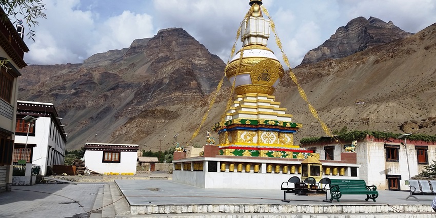 A Gompa with white and golden architecture and a green bench in the complex area