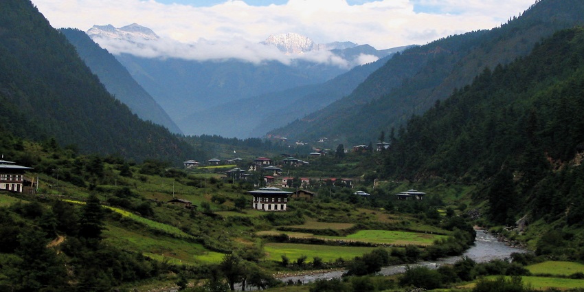 Haa valley with distant traditional buildings & houses, farms, green trees and mountains.