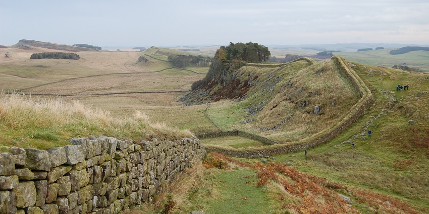 Hadrian’s Wall with a small wall made up of stones, green plains and people at a distance