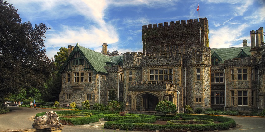 A grand ivy-covered castle with turrets, surrounded by lush greenery, under the clear sky.