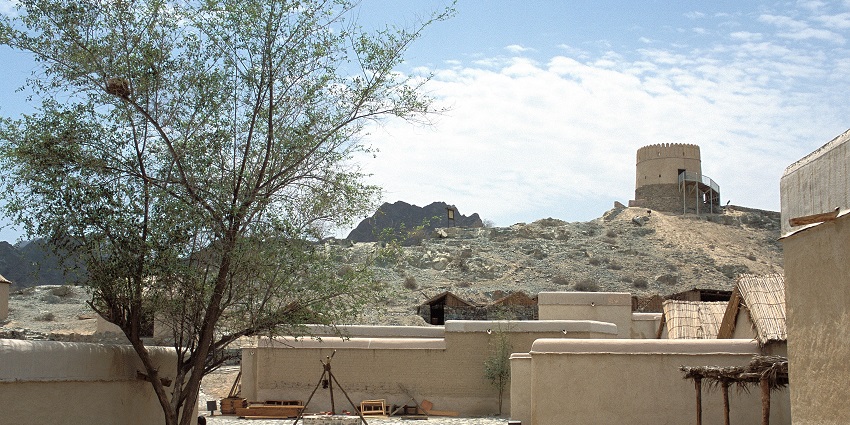 Traditional houses and the Fujairah Fort watchtower on a rocky hill under a partly cloudy sky, one of the historical places in Dubai.