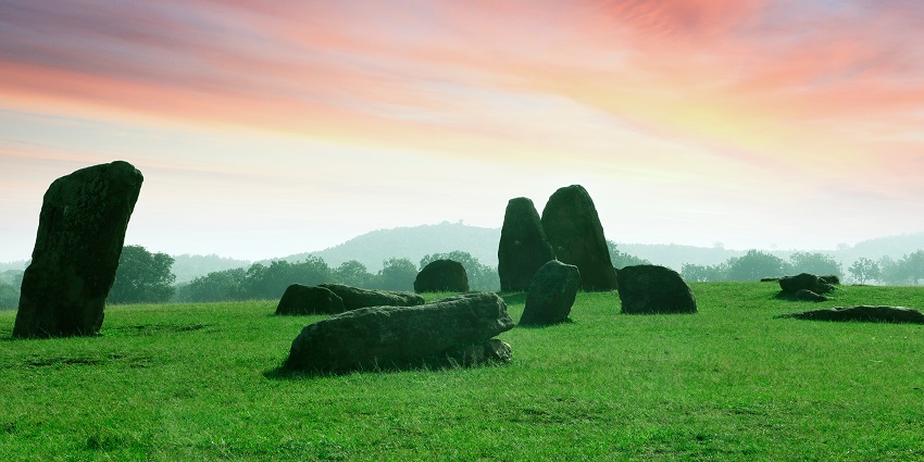 Megaliths in Hazaribagh, surrounded by a dense line of tall green trees under a clear bright sky.