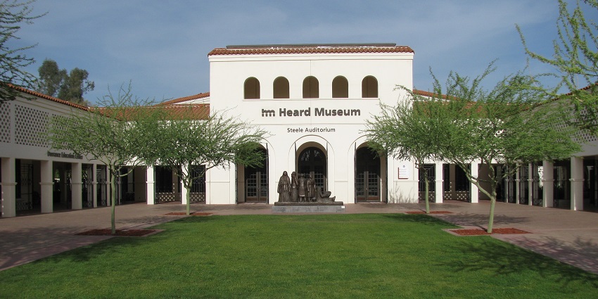 The Heard Museum with an arched entrance, a statue, trees, and a manicured lawn.