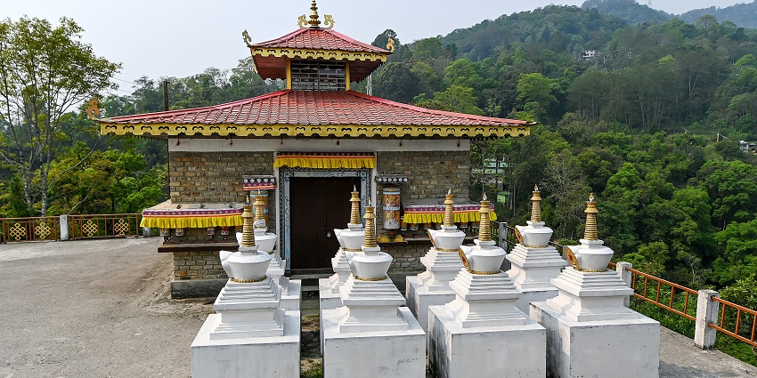 A small Buddhist shrine with a red roof and white stupas stands amid green forested hills, amongst the best places to visit in Sikkim in October.