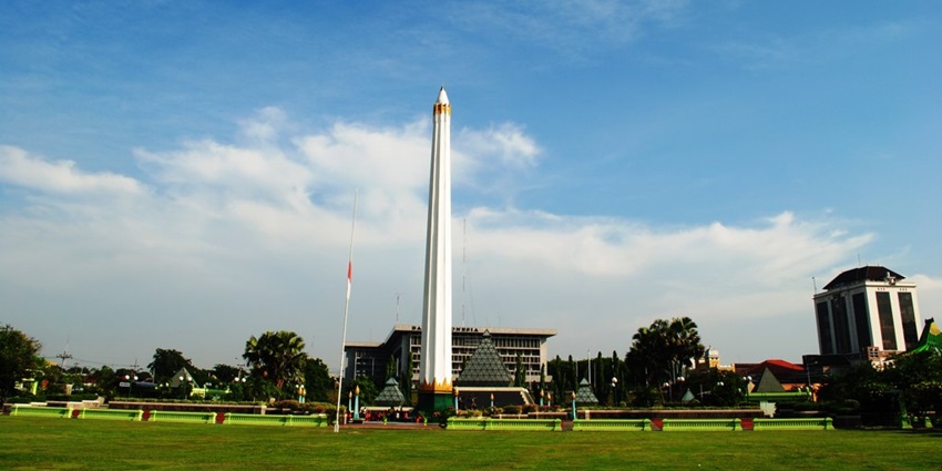 A tall, white obelisk with a gold-tipped peak in a park surrounded by modern buildings and palm trees under a bright blue sky.