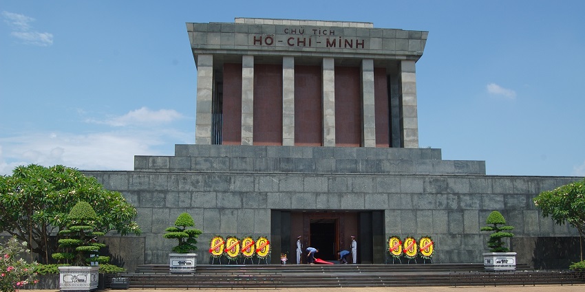 An image of the Ho Chi Minh Mausoleum in Hanoi with Vietnamese flags and a clear blue sky.