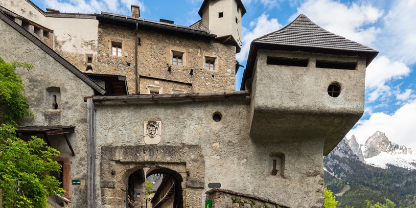 Hohenwerfen Castle is located on a rocky hill surrounded by trees, with a cloudy sky in Werfen, Austria.