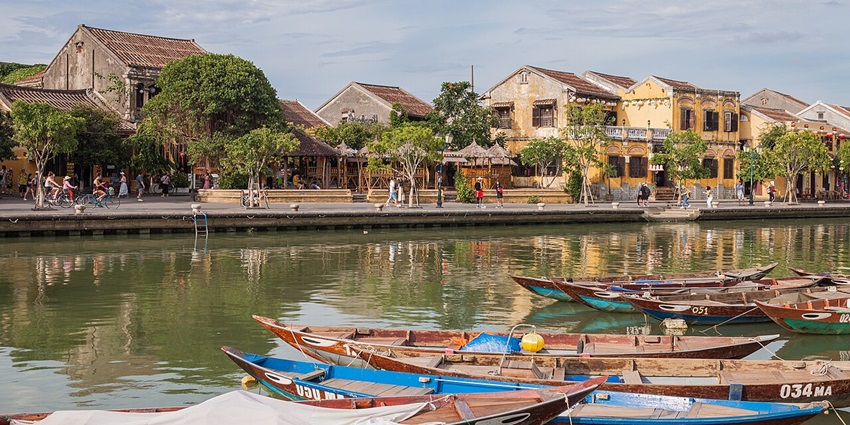 The scenic riverfront of Hội An, Vietnam, with traditional boats docked along the water.