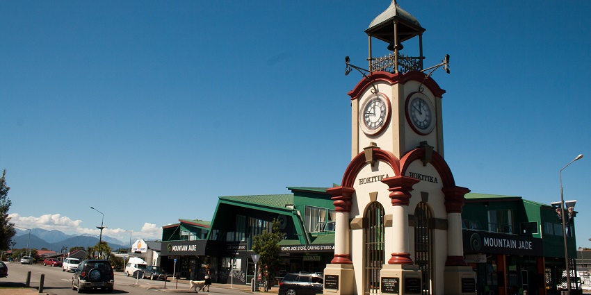 An ornate clock tower with red and cream detailing stands at a street intersection in Hokitika, a prominent historical monument in New Zealand.