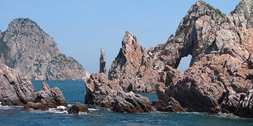 Rocky cliffs and sea caves of Hongdo Island are enveloped in mist and lush vegetation.