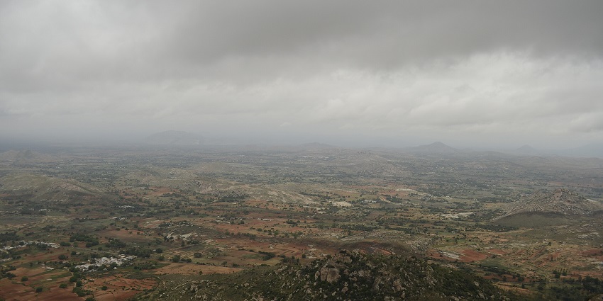 Expansive view of rocky hills and farmlands under a sky with a dramatic overcast mood.