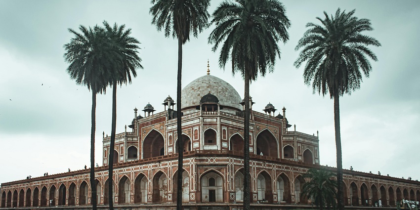 Humayun’s tomb in cloudy weather with traditional white-brown architecture and palm trees.